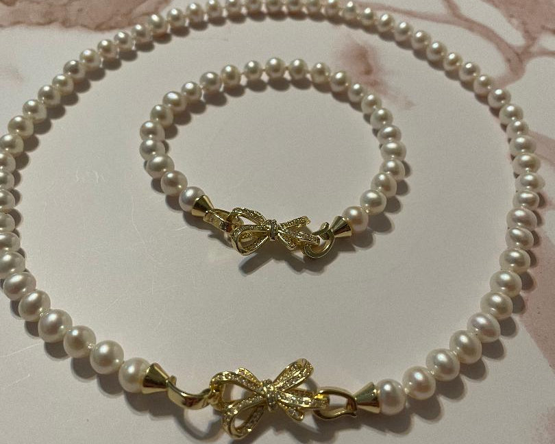 Pearl necklace and bracelet set with gold clasp on a marble surface