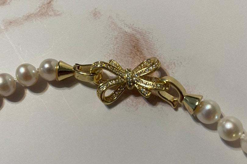 Pearl necklace with a gold bow clasp on a marble surface