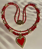 Red beaded necklace with gold heart pendants on a white background