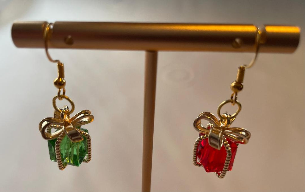 Gold bow-shaped earrings with green and red gemstones on a stand.